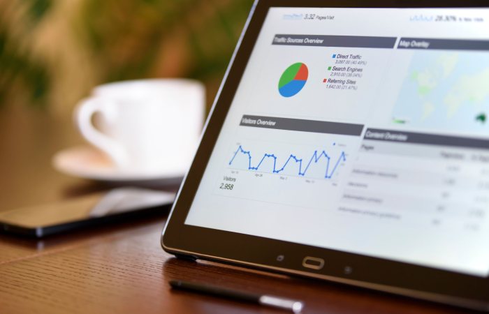 Close-up of a tablet displaying analytics charts on a wooden office desk, alongside a smartphone and coffee cup.