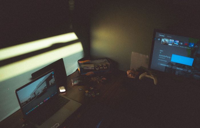 Dark room with a laptop and gaming console creating a moody tech atmosphere.